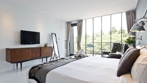 Una camera d'albergo moderna con un letto grande, una TV a schermo piatto, una cassettiera in legno e vista sull'esterno attraverso ampie finestre.