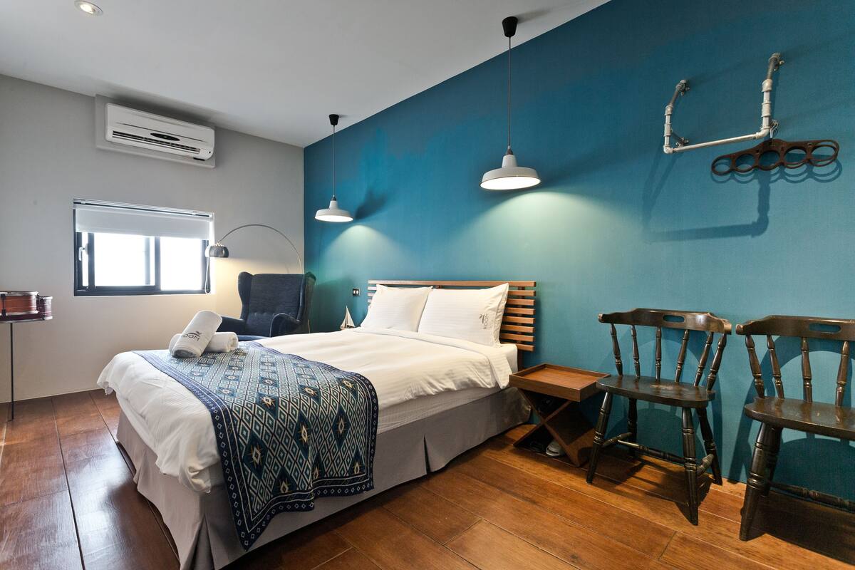 Quarto de hotel com cama, mesas de cabeceira, escrivaninha e duas cadeiras.