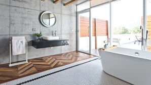 Un bagno moderno con un'ampia finestra, una vasca da bagno indipendente, uno specchio rotondo e un pavimento in legno.