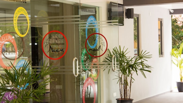 A hotel entrance with glass doors, potted plants, and various circular stickers on the glass. - Naam Boutique Lodge (Port Dickson)
