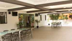 A spacious indoor area with a glass table and chairs, a potted plant, and a view of the outdoors. - Naam Boutique Lodge (Port Dickson)