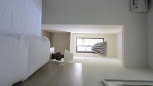 A hotel room with a bed, a small table, a window with a view, and an air conditioning unit. - Naam Boutique Lodge (Port Dickson)