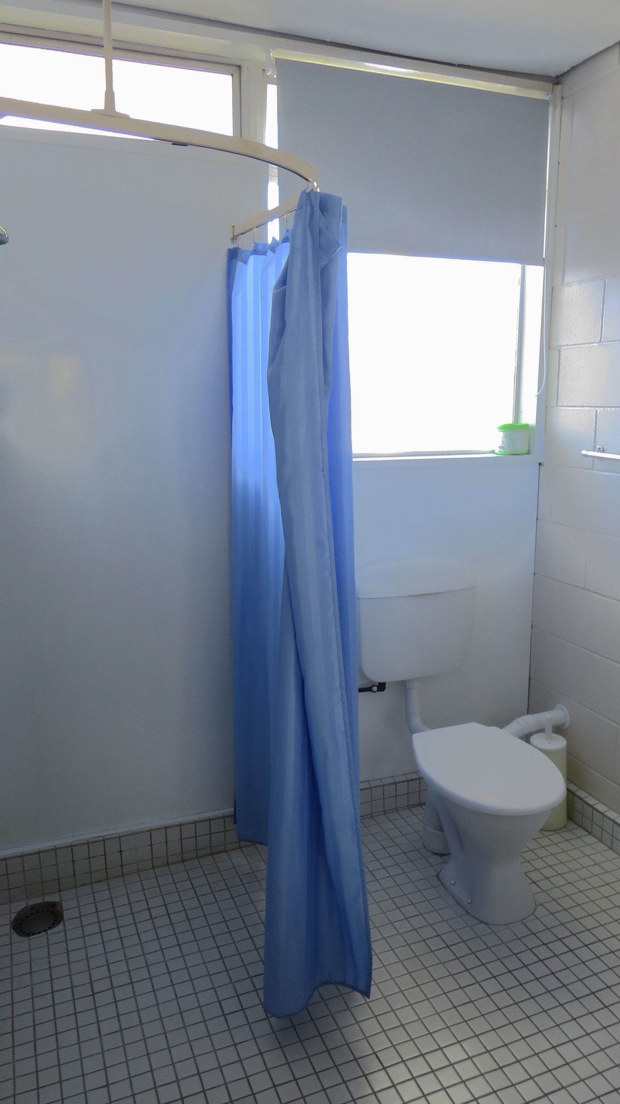 A bathroom with a toilet, a blue shower curtain, and a window.