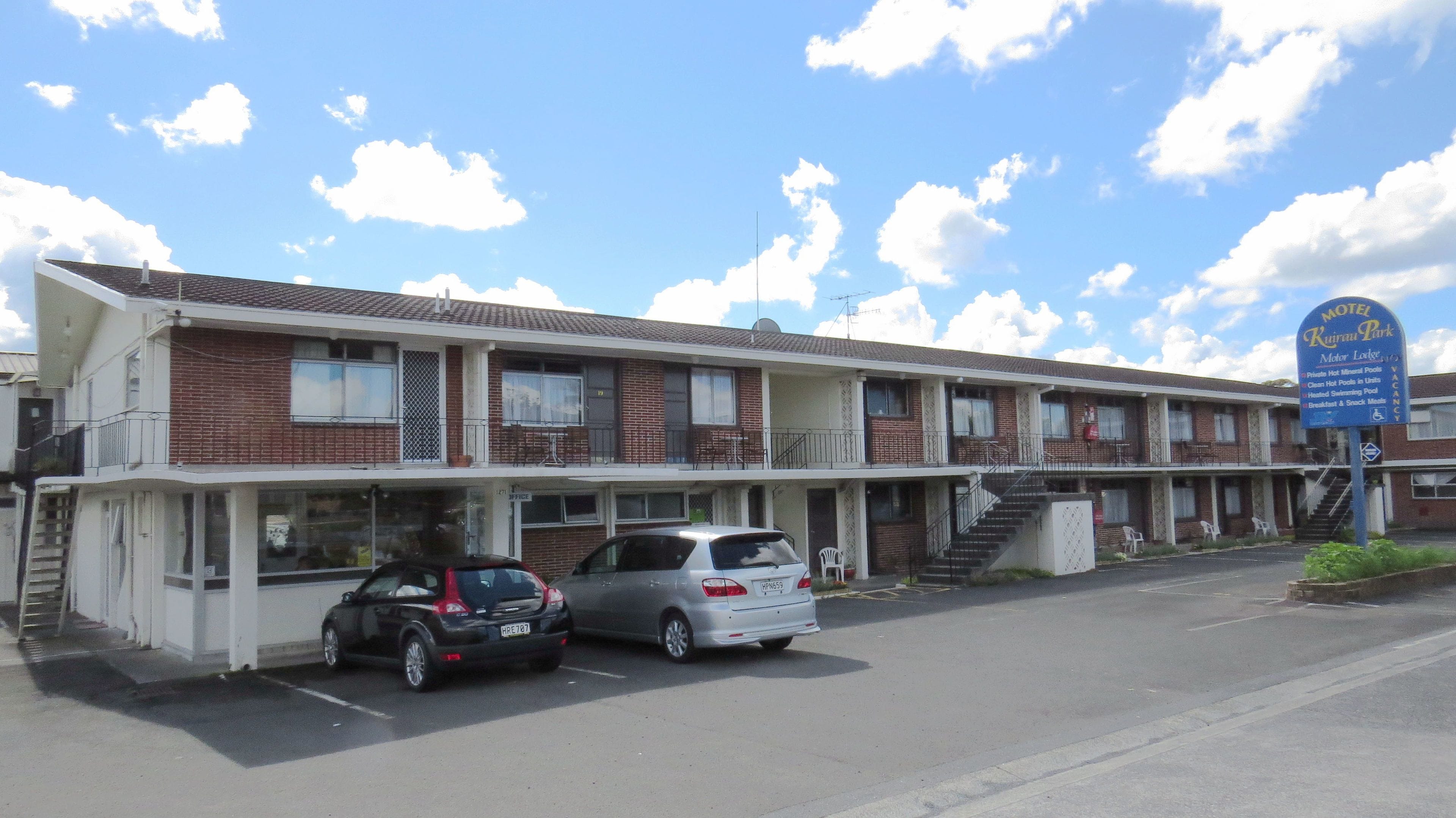 A motel with a two-story structure, a covered parking area, and a signboard advertising amenities like hot mineral pools and a breakfast menu.