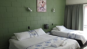 Ein Hotelzimmer mit zwei Betten, grünen Ziegelwänden, einem Gemälde und einem Fenster mit Vorhängen.
