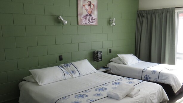 Une chambre d’hôtel avec deux lits, des murs en briques vertes, un tableau et une fenêtre avec des rideaux.