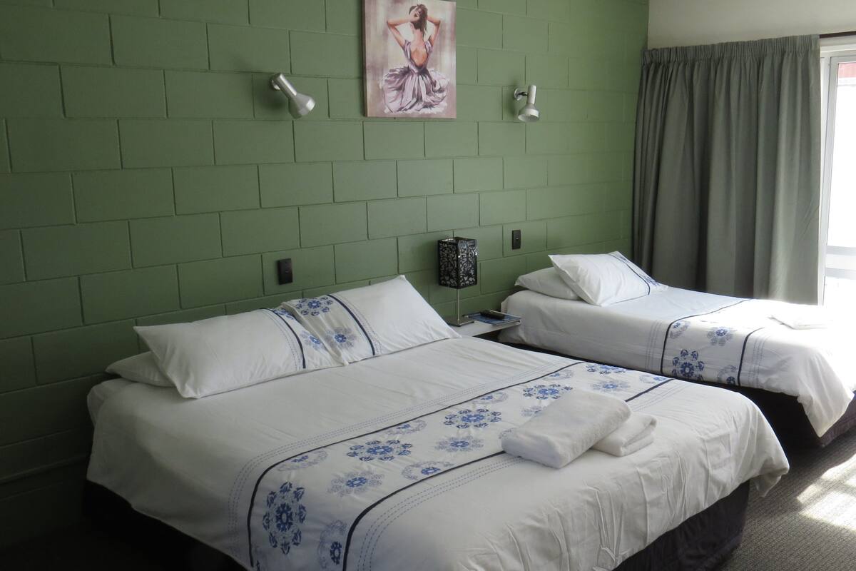 Ein Hotelzimmer mit zwei Betten, grünen Ziegelwänden, einem Gemälde und einem Fenster mit Vorhängen.