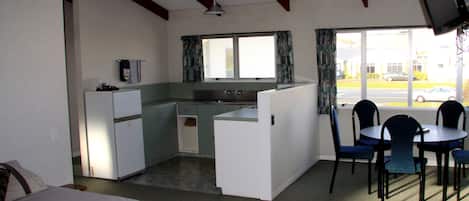 A compact room with a kitchenette, a bed, a dining area with chairs, and a TV mounted on the wall.