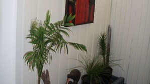 Un couloir aux murs blancs, orné d’un tableau abstrait rouge et agrémenté de plantes en pot.
