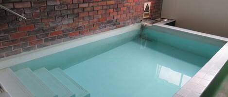 A swimming pool with a brick wall and tiled steps leading into it.