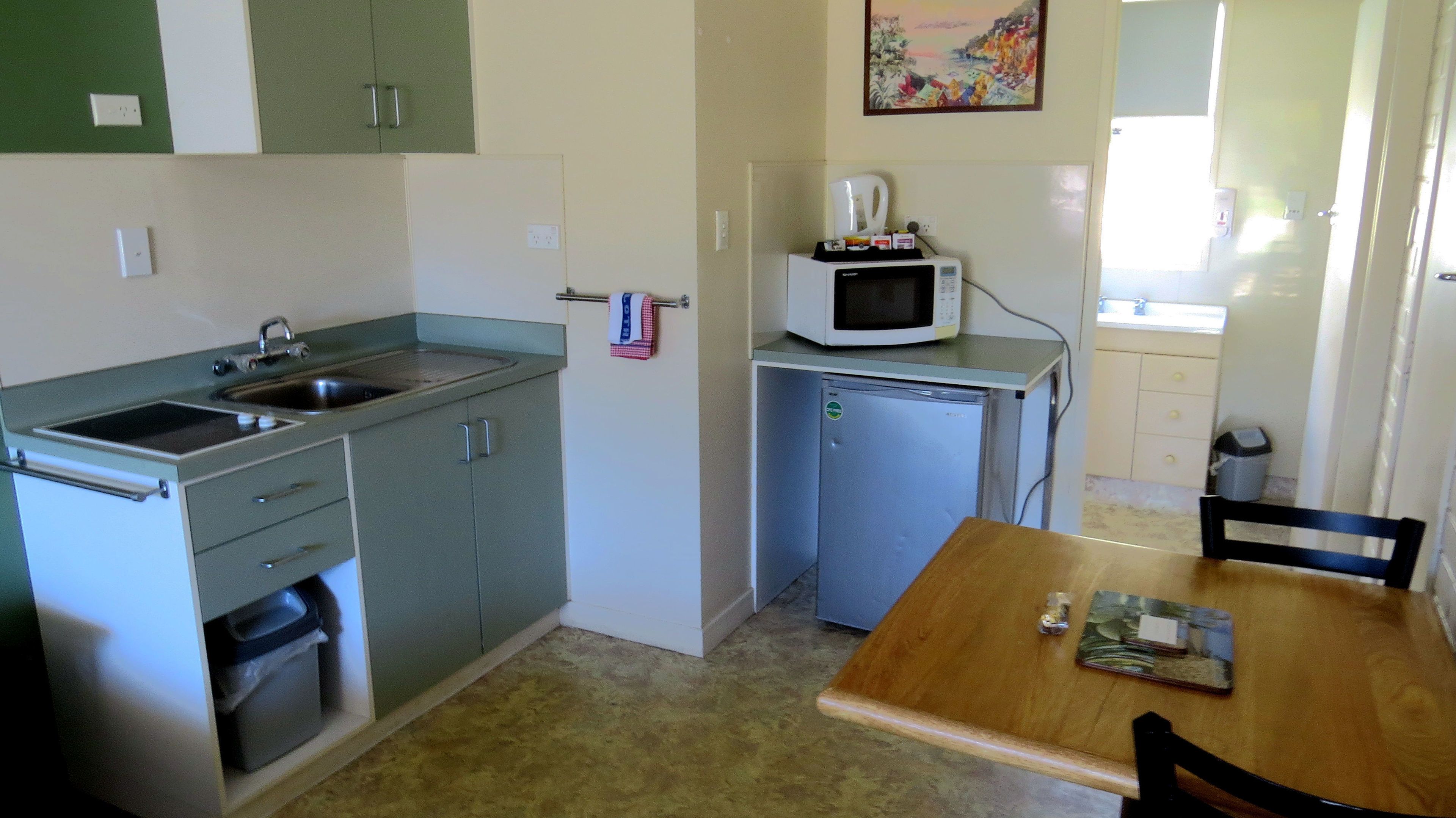 Cocina compacta con un lavamanos, microondas y un refrigerador pequeño. Hay una mesa de comedor con sillas y una ventana que proporciona luz natural.