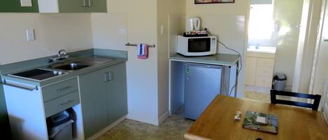 Cocina compacta con un lavamanos, microondas y un refrigerador pequeño. Hay una mesa de comedor con sillas y una ventana que proporciona luz natural.
