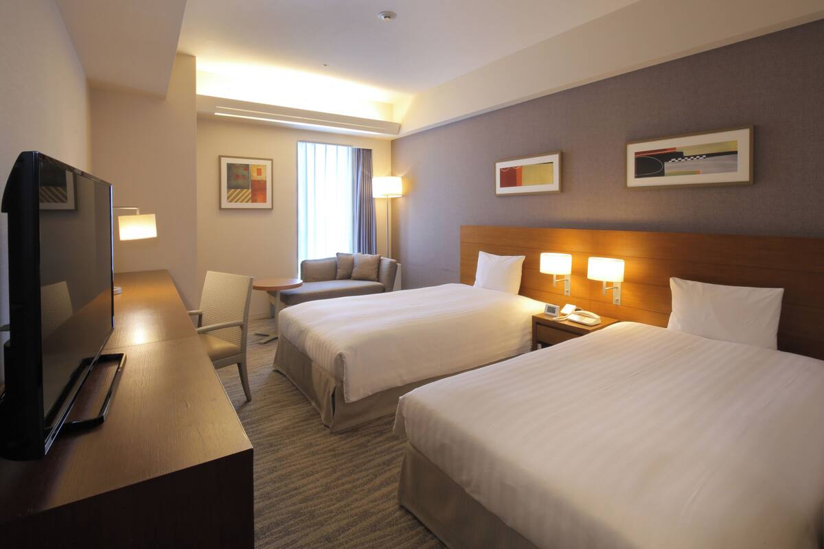 Ein Hotelzimmer mit zwei Betten, einem Schreibtisch, einem Stuhl, einem Fernseher und einer Lampe.