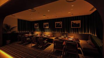A dimly lit restaurant with wooden furniture, dark curtains, and framed pictures on the wall.