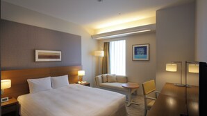 Una habitación de hotel con una cama grande, un escritorio, una silla, un sofá y dos lámparas.