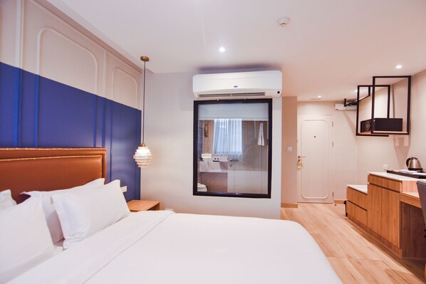 A hotel room with a large bed, a desk with a chair, a mirror, and an air conditioning unit. - THEE Bangkok by TH District (Bangkok)