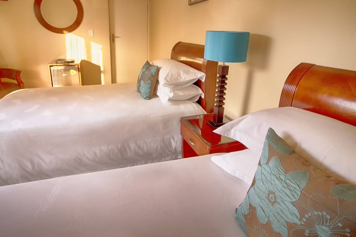 Habitación de hotel con dos camas, cabecero de madera, una silla roja, una mesita y una lámpara.