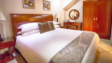 Una habitación de hotel con una cama grande, un cabecero de madera, una mesita de noche con una lámpara, un aparador, un espejo y un armario.
