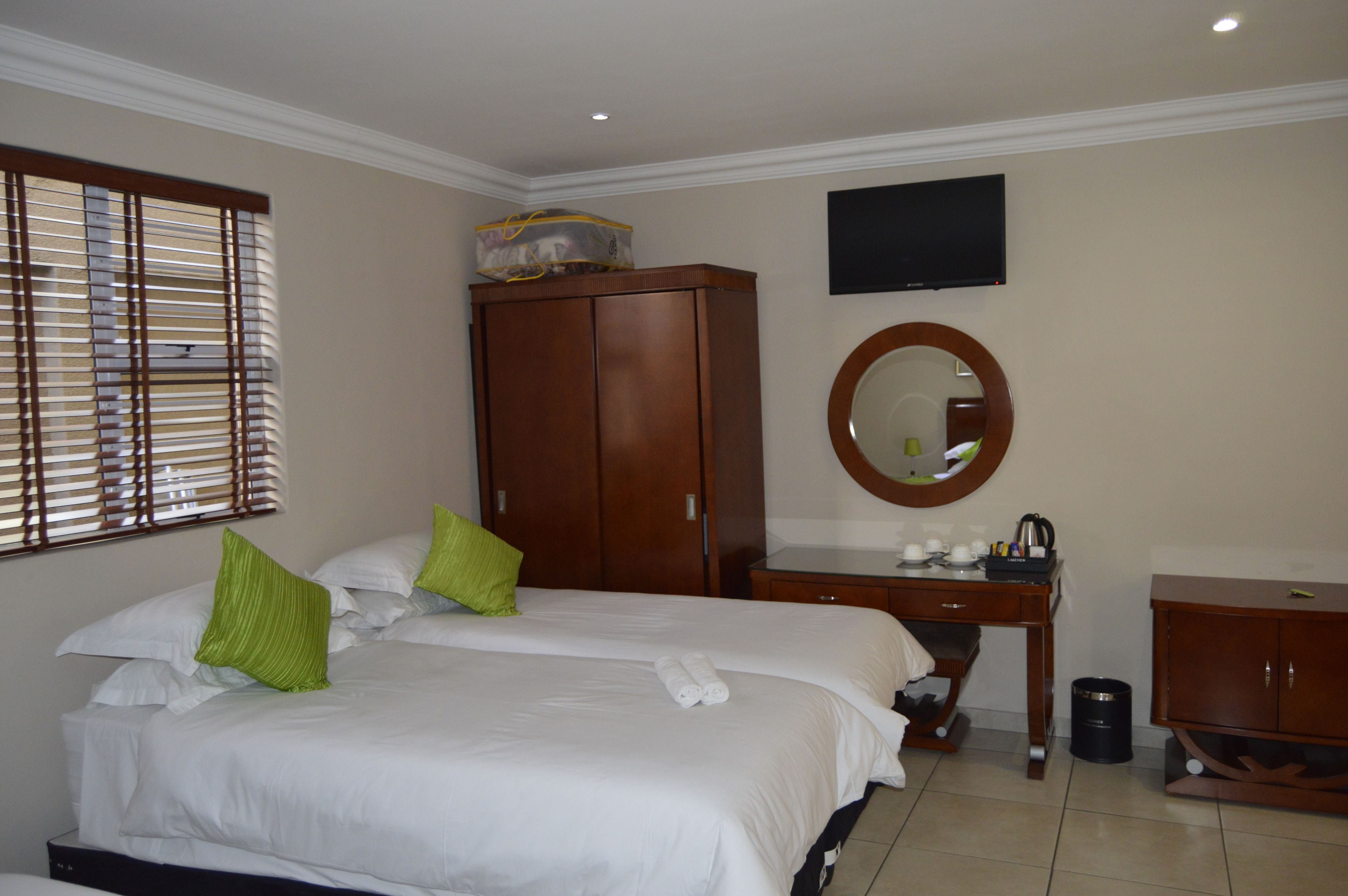 A hotel room with a large bed, a wooden wardrobe, a desk with a mirror, and a television on the wall.