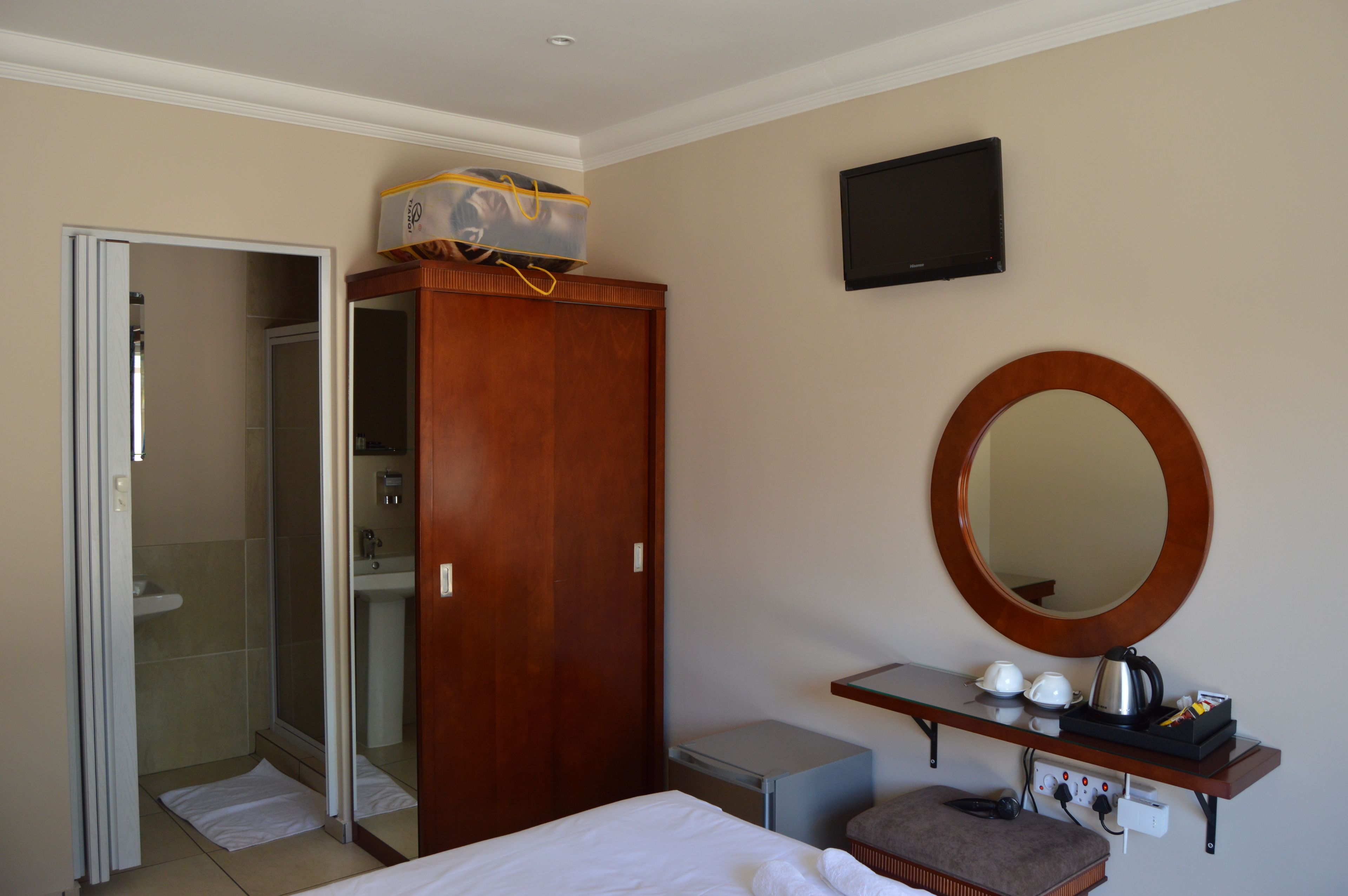 A hotel room with a wooden wardrobe, a mirror, a television, a small table with cups and a kettle, and a shower area.