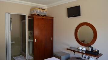 A hotel room with a wooden wardrobe, a mirror, a television, a small table with cups and a kettle, and a shower area.