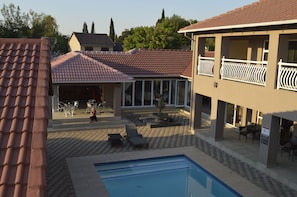 Zona de piscina con sillas de descanso y una fuente, rodeada de edificios con techos de tejas rojas y un porche cubierto.