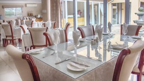 A spacious dining area with a glass table, white chairs, and a view of the outside.