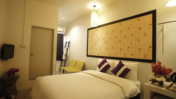 A hotel room with a bed, a TV, a chair, a desk with a vase of flowers, and a wall with calligraphy. - Walking Street Residence (Chiang Mai)