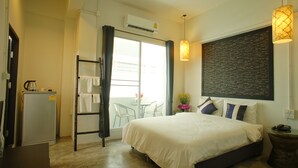 A hotel room with a bed, a desk, a chair, a refrigerator, a window with curtains, and a wall with a chalkboard. - Walking Street Residence (Chiang Mai)