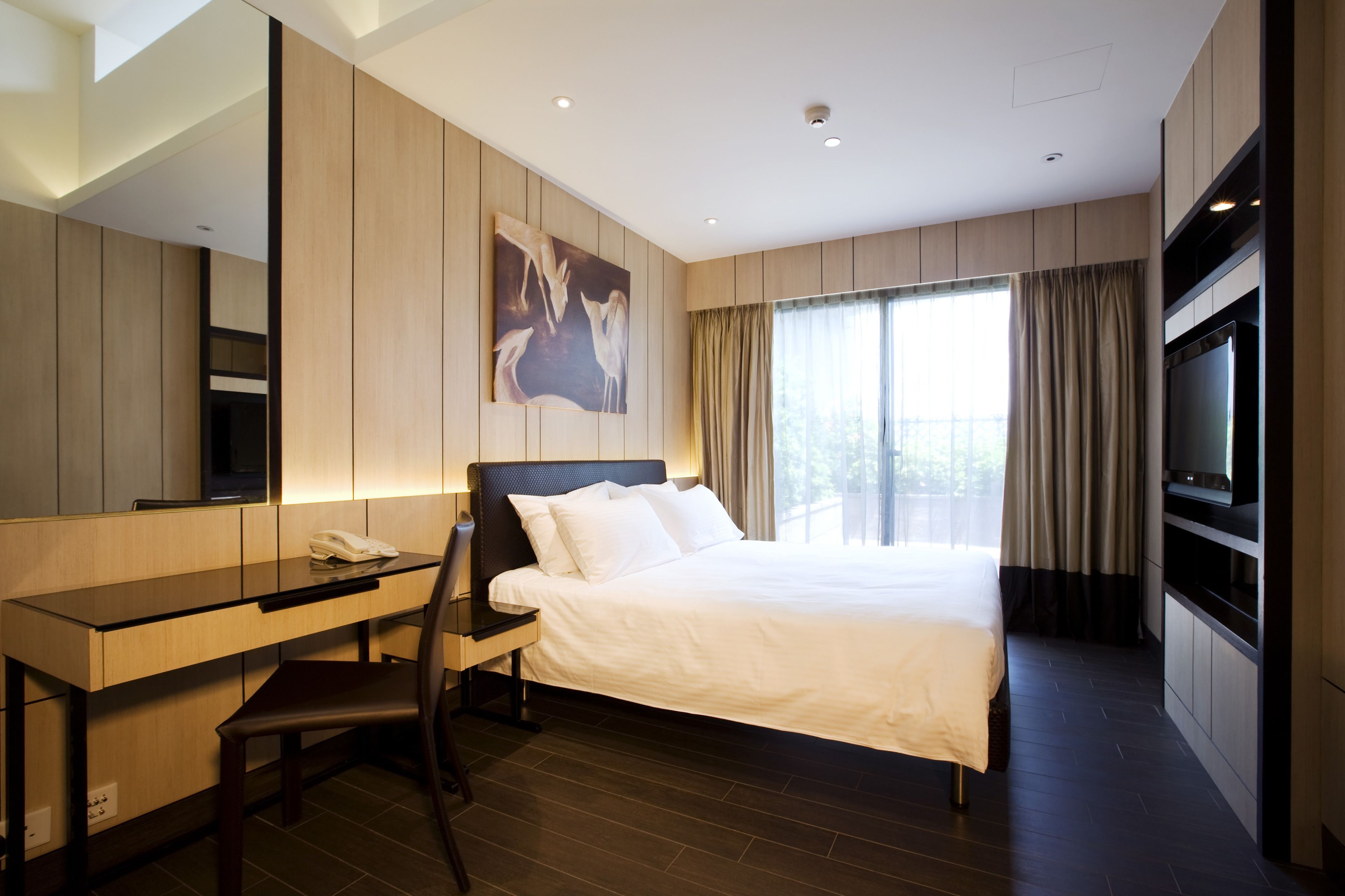 A hotel room with a bed, a desk, a chair, a TV, and a large window with curtains.
