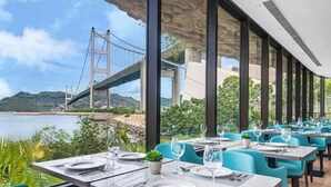 Un restaurante con terraza al aire libre que ofrece vistas a un puente y al agua. Las mesas están dispuestas con platos blancos, cubiertos y copas.