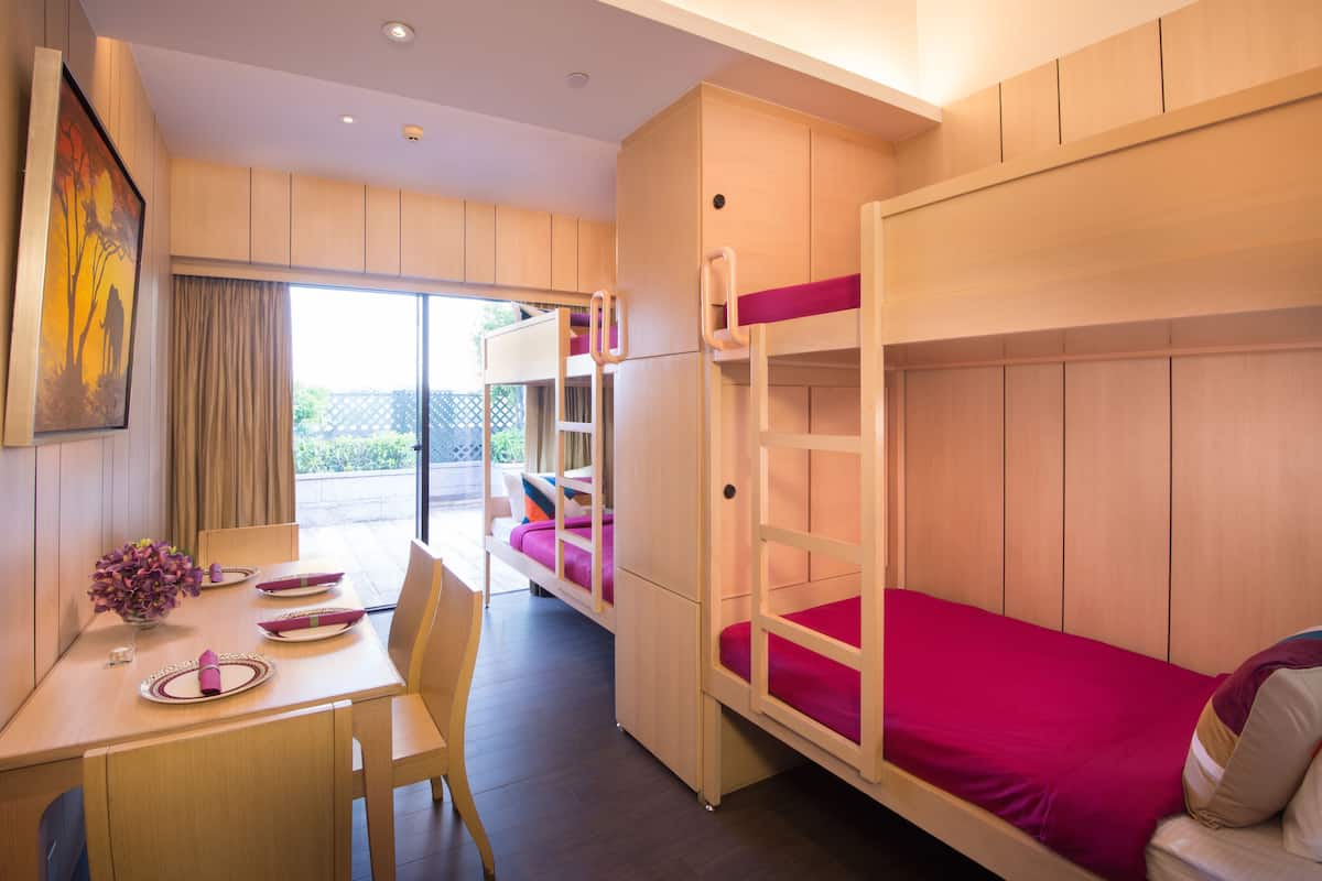 Een kamer met stapelbedden, een eettafel met stoelen en uitzicht door een glazen deur.