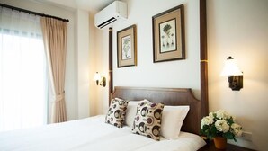 A hotel room with a bed, two wall-mounted lamps, a nightstand with a book and a flower vase, and a window with curtains. - La Pillow8 (Chiang Mai)