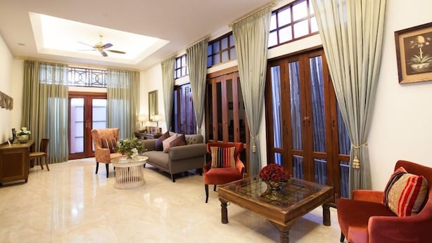A spacious living room with a high ceiling, a ceiling fan, and large windows with curtains. There are several pieces of furniture including a sofa, armchairs, and a coffee table. - La Pillow8 (Chiang Mai)