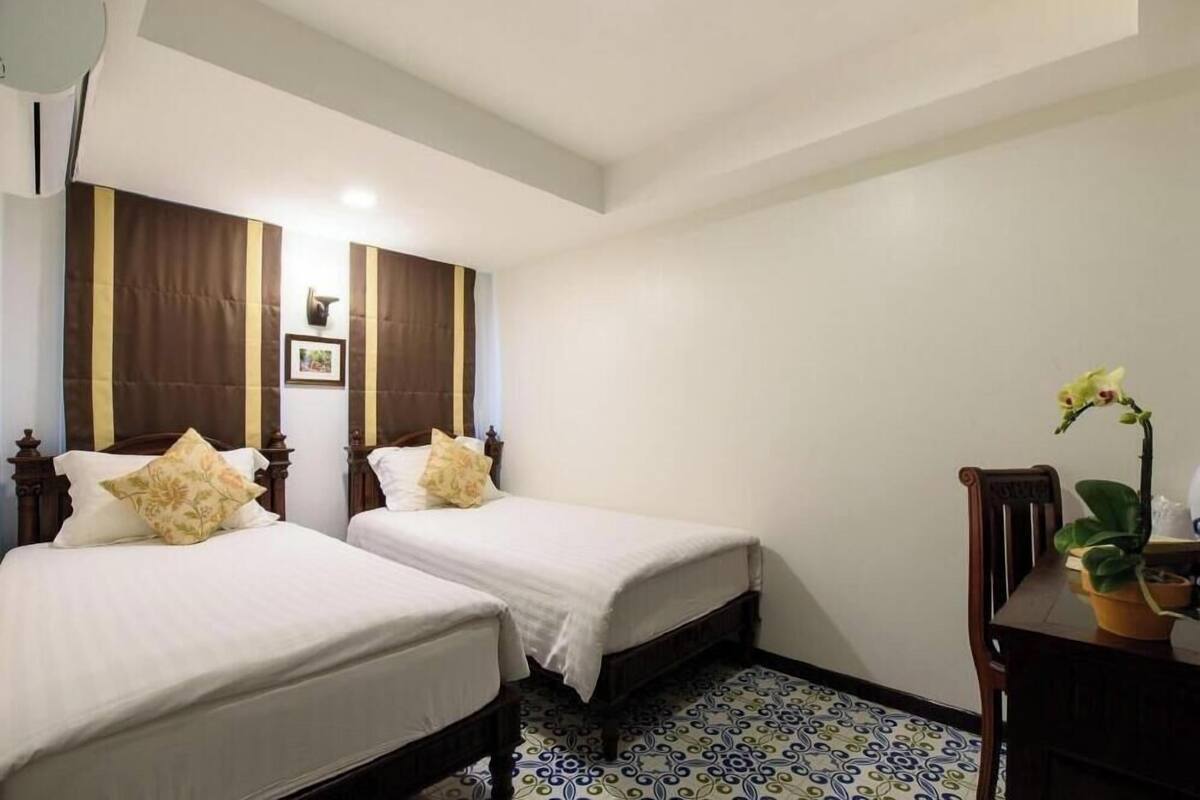 A hotel room with two beds, a wooden headboard, a small table with a potted plant, and a patterned floor.