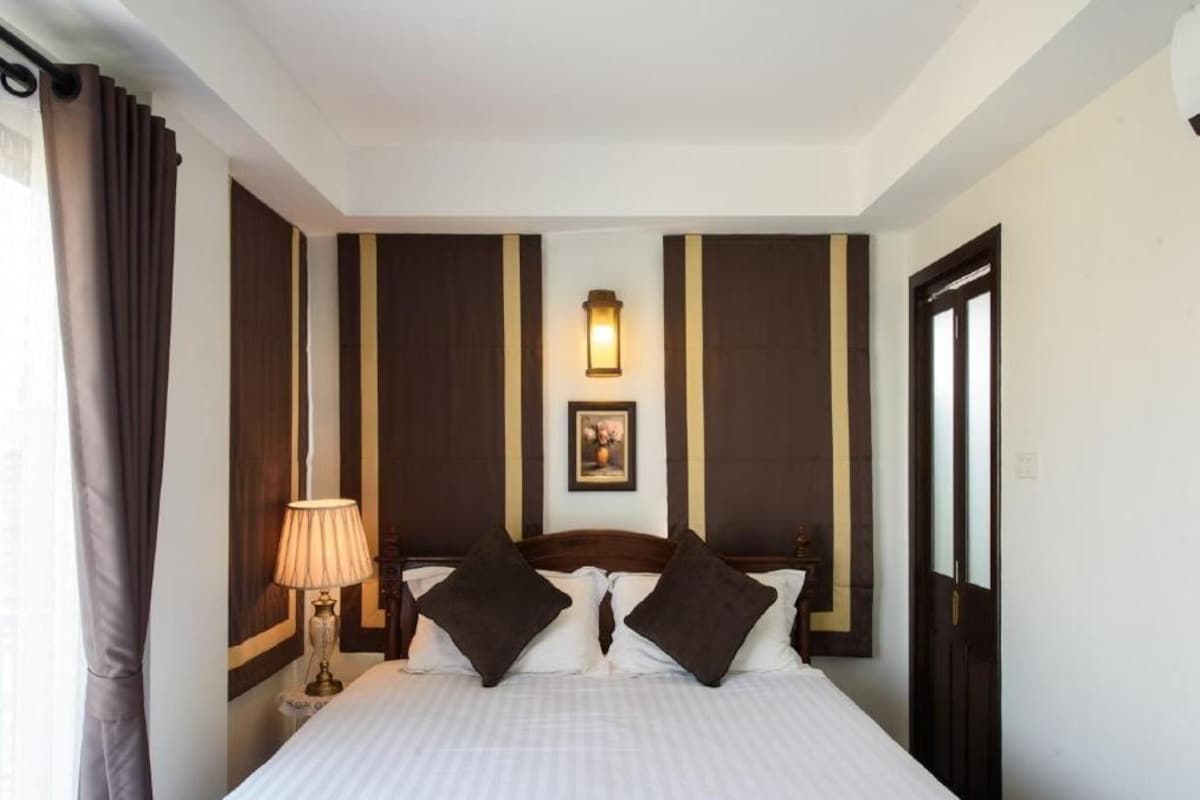 A hotel room with a bed, curtains, a lamp, and a wall-mounted light fixture.