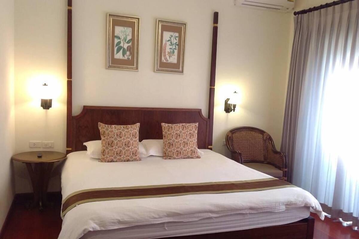 A hotel room with a large bed, two wall-mounted lamps, a wooden headboard, a round side table, and a chair.