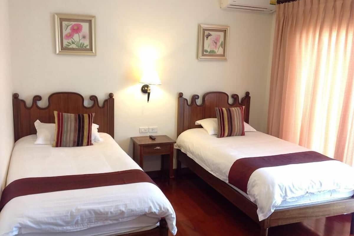 Two double beds with wooden headboards, a bedside table with a lamp, and a wall-mounted air conditioner.