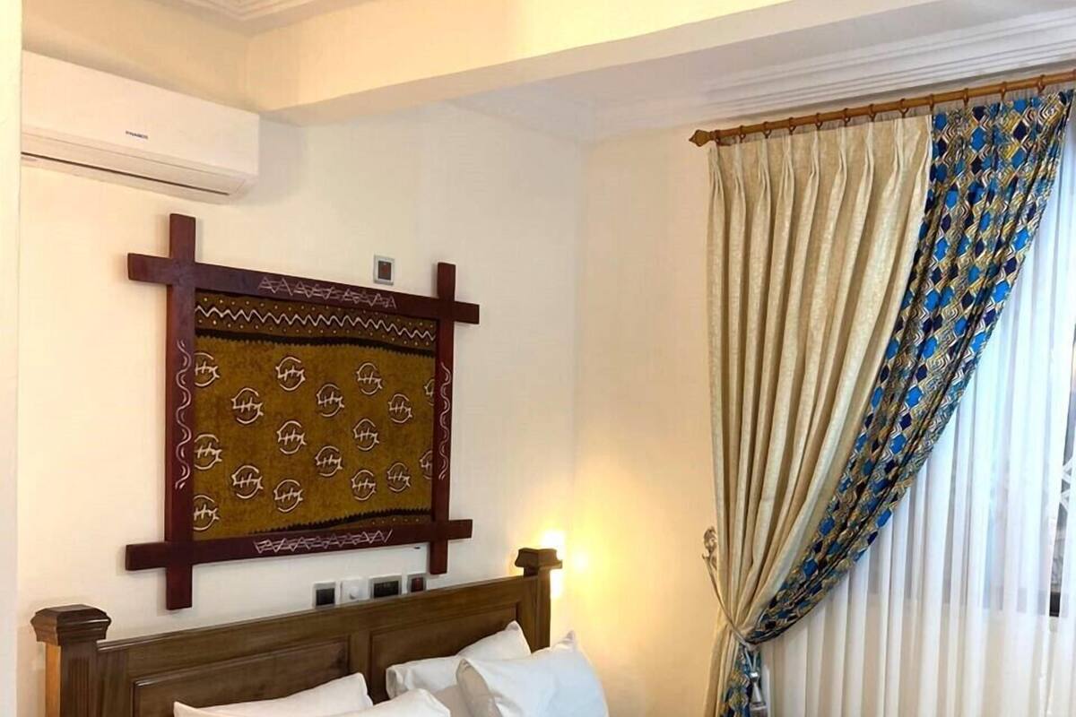 A neatly made bed with white and gray linens, a wooden headboard, and a decorative wall hanging above it.