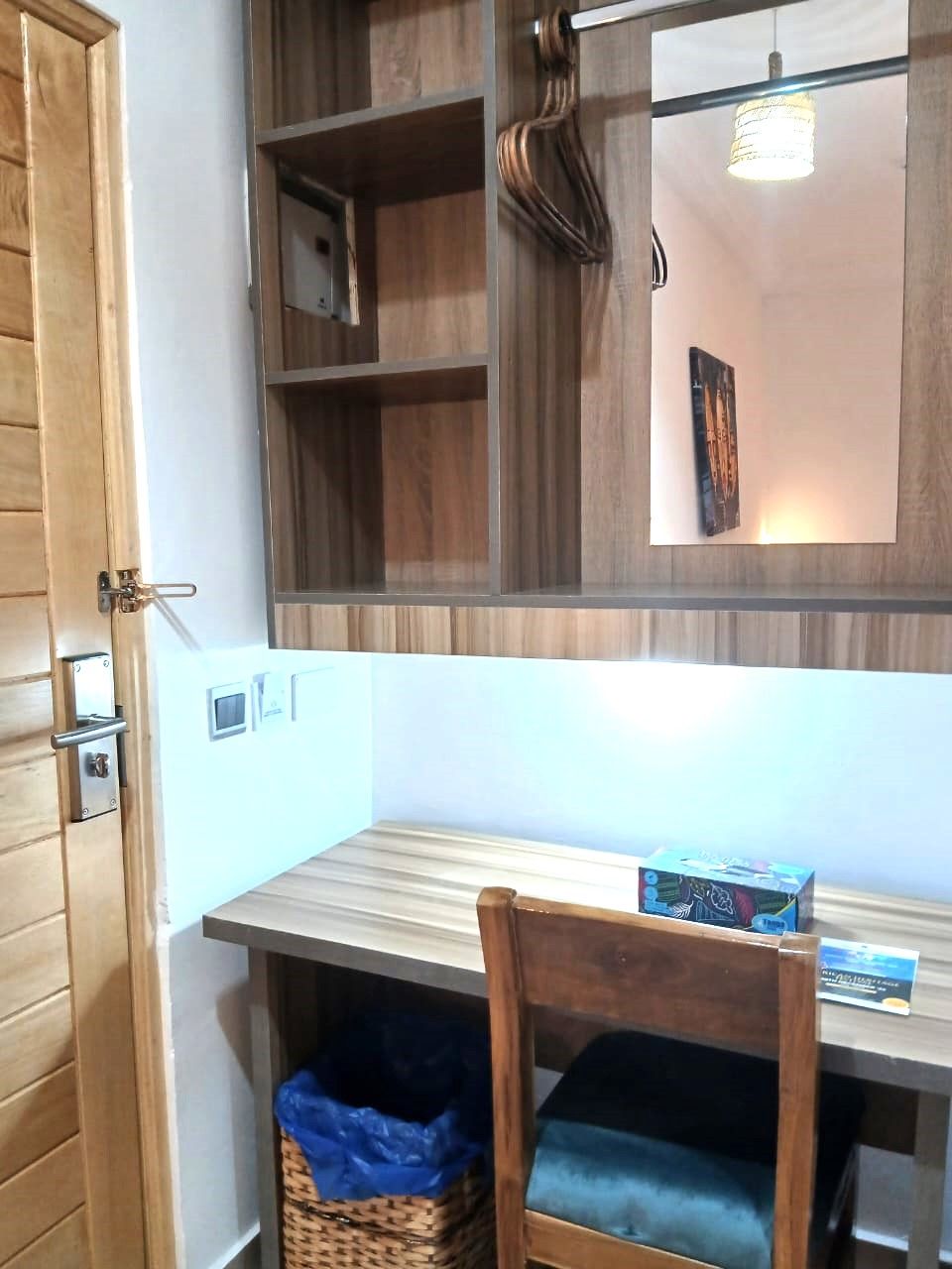 A room with a wooden desk, a chair, a mirror, and a hanging light fixture.