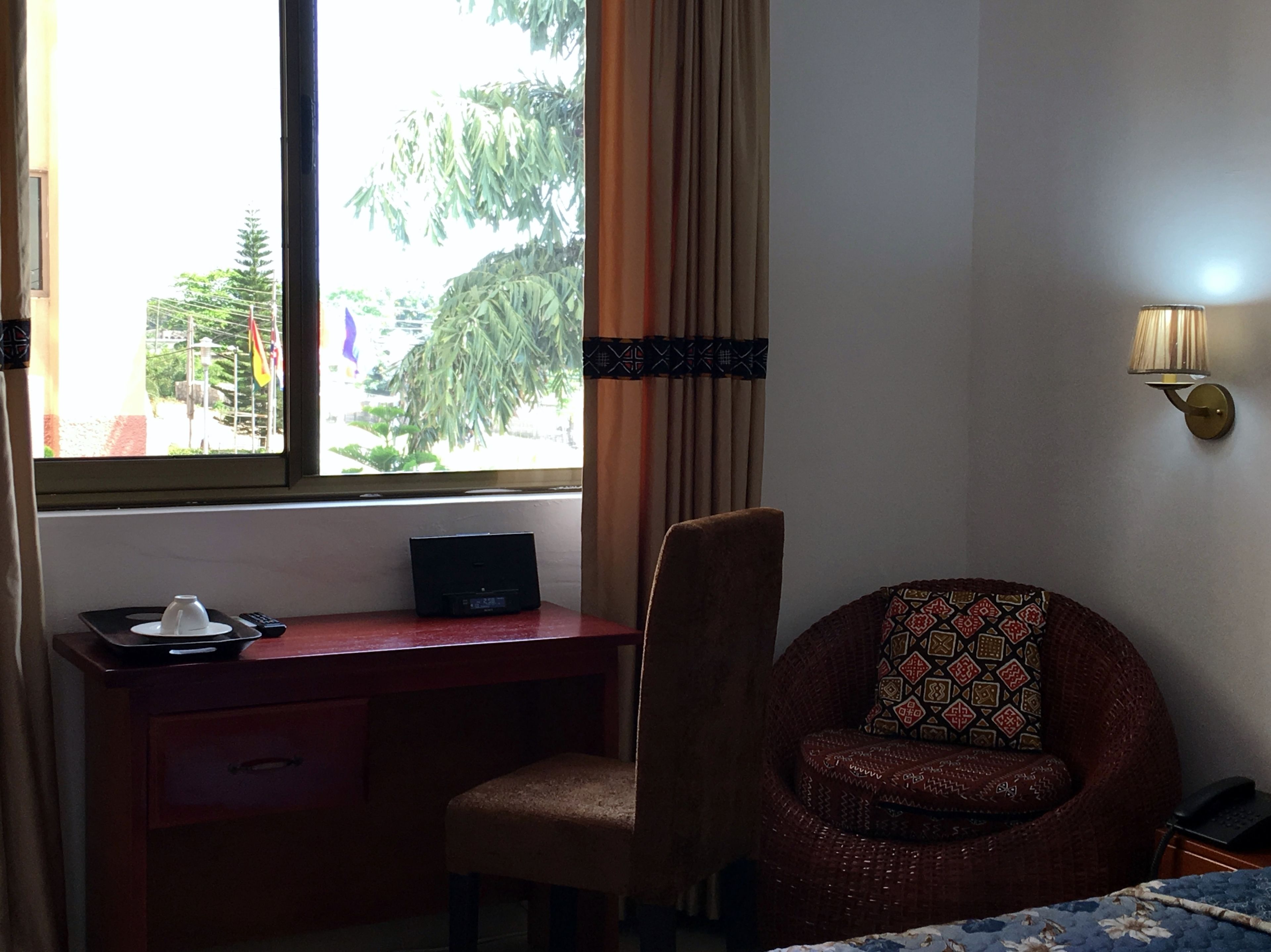 A hotel room with a desk, chair, and a view of trees through the window.