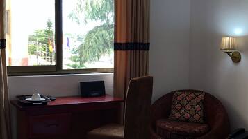 Habitación de hotel con escritorio, silla y vista a los árboles a través del ventanal.