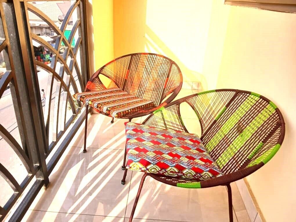 Zwei Korbstühle mit bunten Kissen auf einem Balkon mit Metallgeländer.