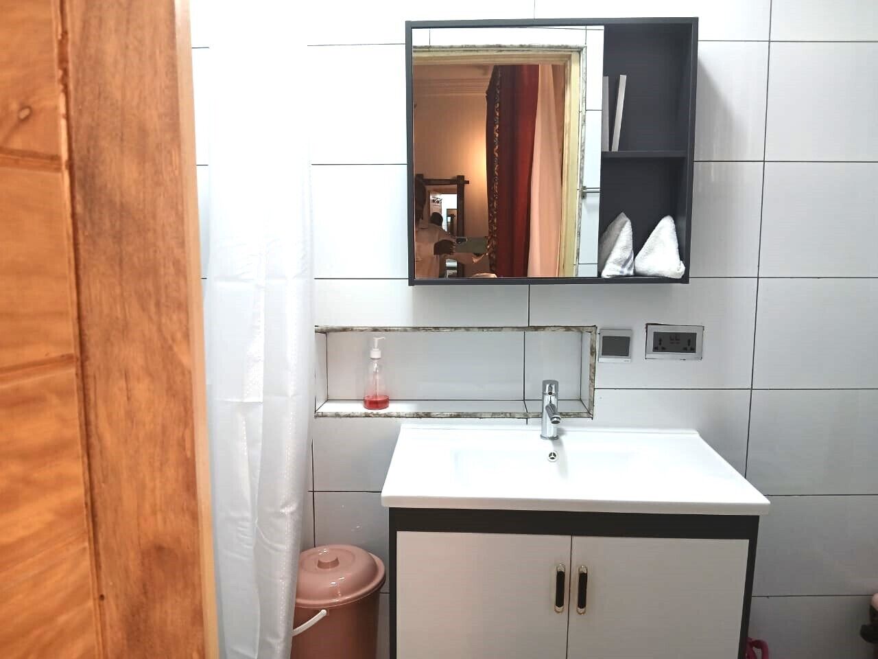 A bathroom with a white sink, a mirror above it, and a shelf with toiletries.