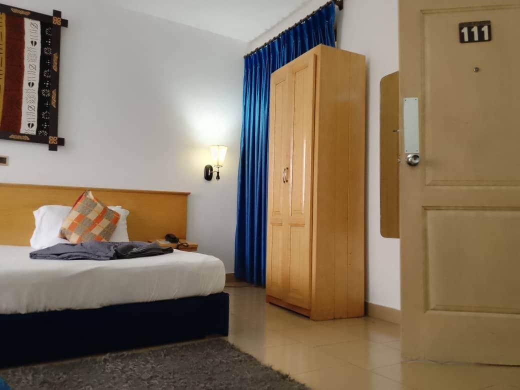 A hotel room with a bed, a wardrobe, a door with the number 111, and a wall-mounted light fixture.