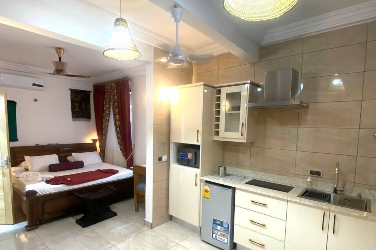 A compact hotel room with a bed, bedside table, and a small kitchenette.