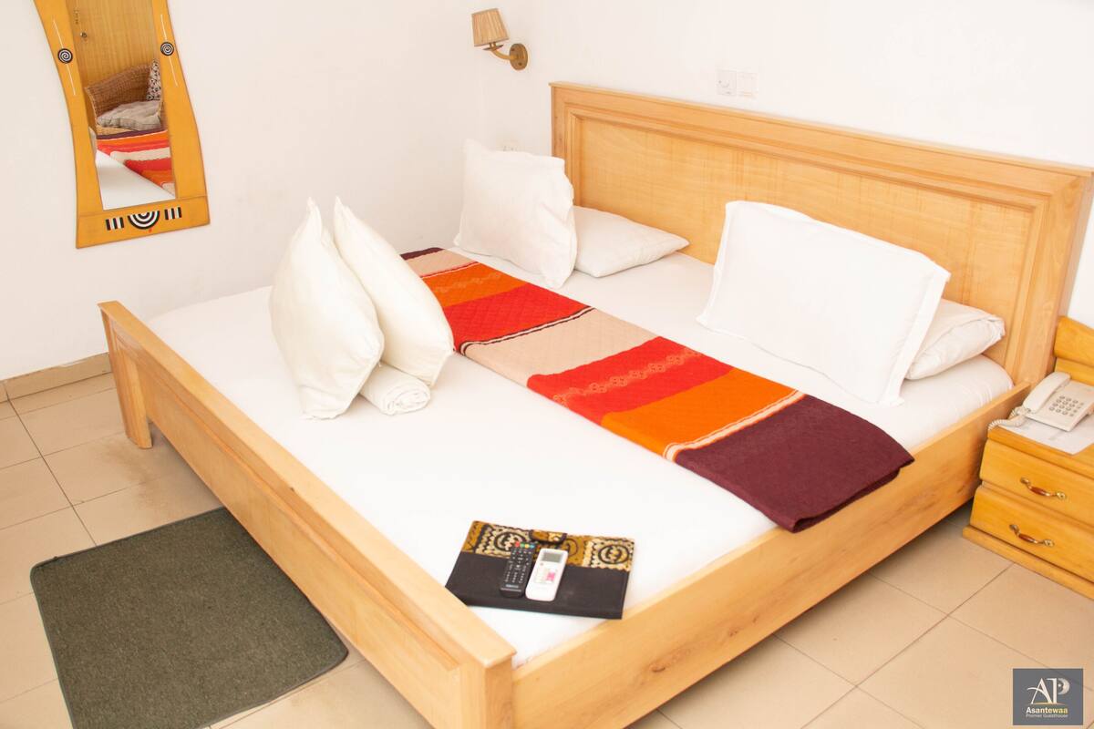 A neatly made bed with white and red blankets, a wooden headboard, and a bedside table with a lamp.