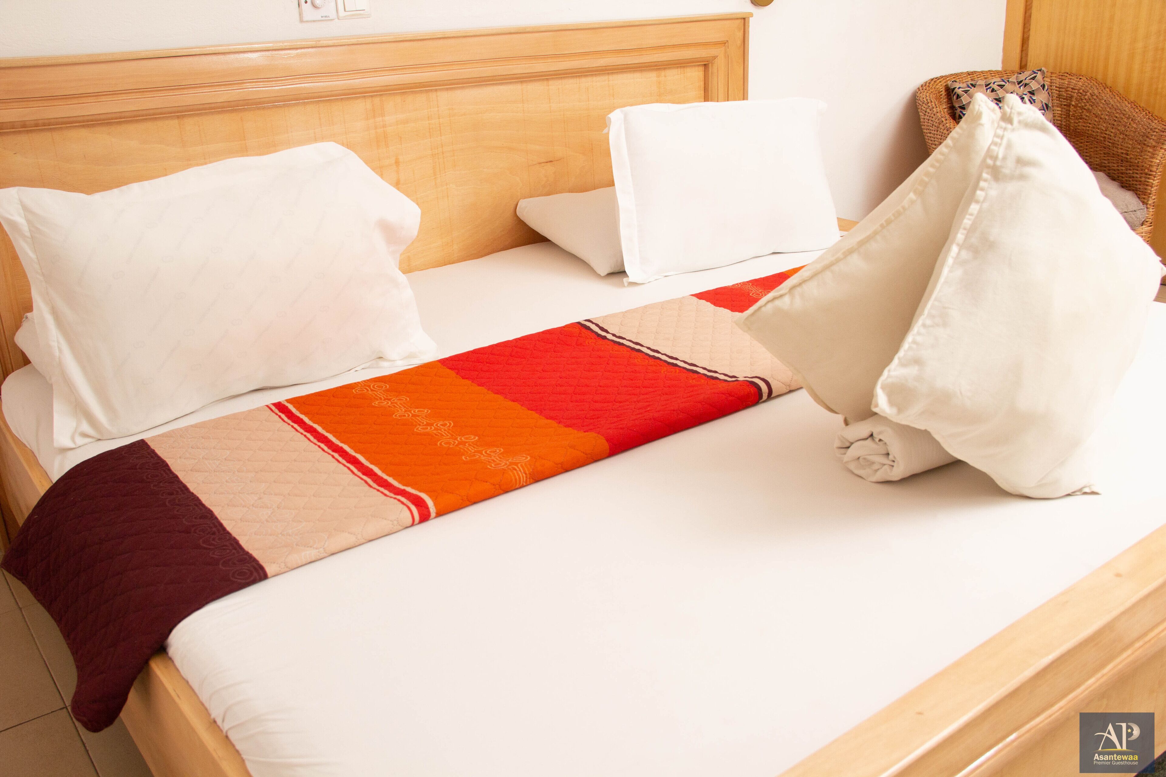A neatly made bed with white linens, a red and beige blanket, and two white pillows.