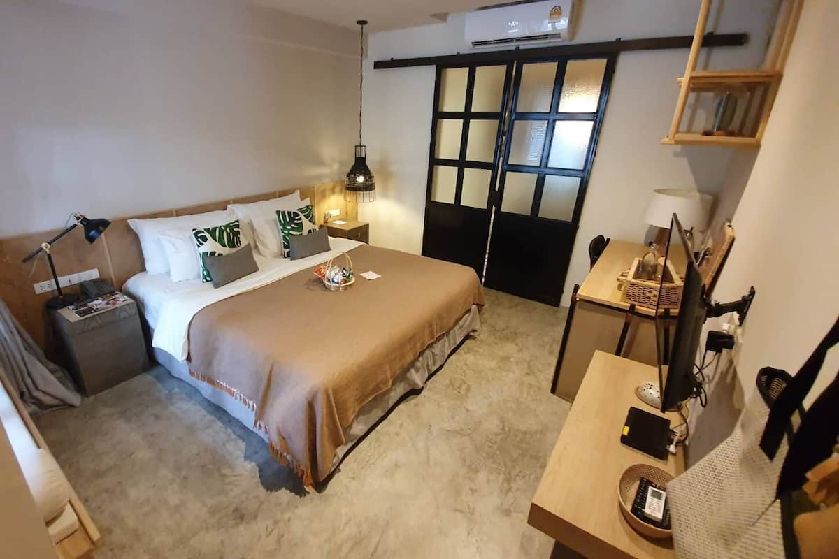 Una habitación de hotel con cama, mesita de noche, lámpara y escritorio con computadora.