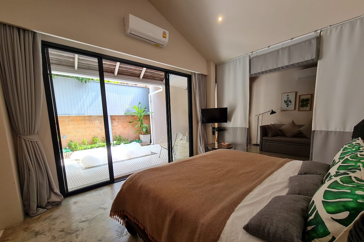 Un dormitorio con una cama grande, televisor, sofá y puerta corrediza de vidrio que da a un patio.
